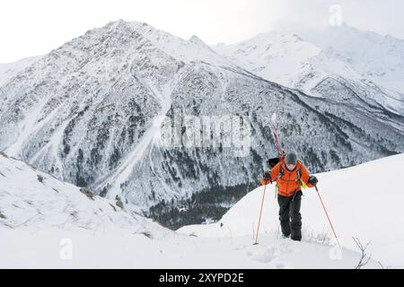 Der Ski-Freerider klettert die Piste in Tiefschneepulver, wobei die Ausrüstung auf der Rückseite auf dem Rucksack befestigt ist. Das Konzept des Winterextremen Sports Stockfoto