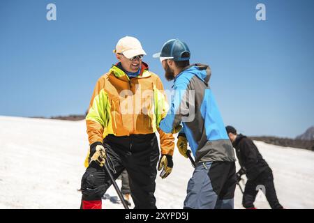 Training zum Korrigieren des Rutschens an Hanglagen oder Gletschern mit Hilfe einer Eispistole. Ein junger Reiseleiter mit Bart erklärt seiner Gruppe, wie man das richtig verlangsamt Stockfoto