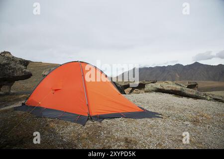 Ein orangenes Hochgebirgszelt befindet sich zwischen Steinen hoch in den Bergen des Kaukasus vor dem Hintergrund des Kaukasus. Glade aus Stein m Stockfoto