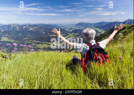 Frau sitzt auf einer Bergwiese und schaut ins Tal Stockfoto