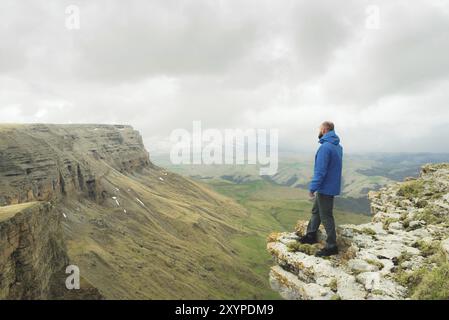 Bärtiger Hipster-Tourist, der am Felsenrand steht und auf einem epischen Plateau in die Ferne blickt. Das Konzept des Tourismus Stockfoto