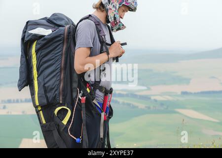 Nahaufnahme eines professionellen Gleitschirms mit einem Kokon auf den Schultern Knöpfe Helm sieht zur Seite. Gleitschirmsportkonzept Stockfoto