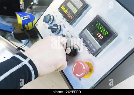 Eine Nahaufnahme der Hand eines Mannes hält einen Drehschalter auf der Bedienkonsole mit Instrumenten Stockfoto