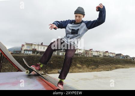 Ein Teenager-Skateboarder mit Hut macht einen Rocks-Trick auf einer Rampe in einem Skatepark vor bewölktem Himmel und Schlafbereich. Das Konzept des urbanen Stils in sp Stockfoto