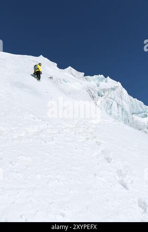 Ein Skifahrer in Helm und Maske mit Rucksack steigt auf einer Piste vor dem Hintergrund von Schnee und einem Gletscher. Backcountry Freeride Stockfoto