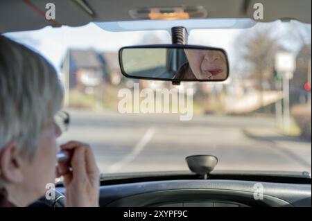 Eine ältere Dame rollt in ihrem Auto zu einem Kreuz und berührt ihren Lippenstift Stockfoto