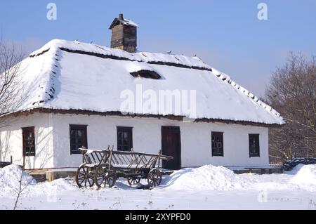 Altes hölzernes Landhaus mit einem Strohdach bedeckt mit Schnee und einem Wagen auf dem Hof Ukraine Osteuropa Winter landschaftlich Horizontal OR Stockfoto