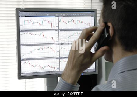 Person sitzt im Büro und spricht mit Handy vor einem Display, das Forex Devisenkerzendiagramme zeigt Forex Trader Online com Stockfoto