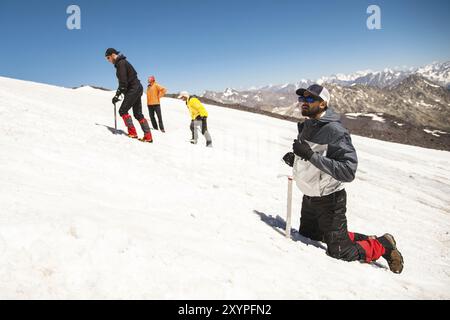 Training zum Korrigieren des Rutschens an Hanglagen oder Gletschern mit Hilfe einer Eispistole. Ein voll ausgestatteter Backpacker kniet auf einem schneebedeckten Hang in den Bergen in der Nähe Stockfoto