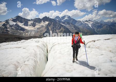 Bergsteigerin genießt die Schönheit des Gletschers Spaziergänge auf dem Gletscher im Steigeisen und in der Sonnenbrille. Vor dem Hintergrund der hohen Berge o Stockfoto