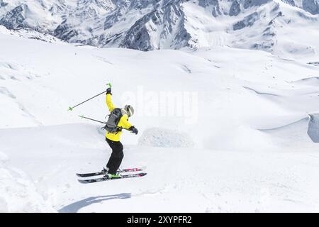 Ein Skifahrer in voller Sportausrüstung springt von der Spitze des Gletschers in den Abgrund vor dem Hintergrund des blauen Himmels und der kaukasischen Schnee-Ca Stockfoto