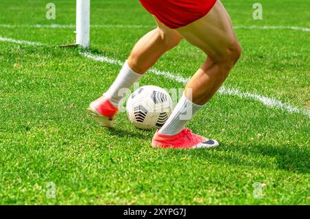 Junge Fußballspieler werden auf einem grünen Feld in Aktion gesehen. Der Spieler, der in roten Shorts gekleidet ist, kontrolliert den Fußball. Stockfoto