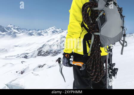 Ein Bergsteiger hält eine Eisaxt hoch in den Bergen, die mit Schnee bedeckt sind. Nahaufnahme von hinten. Outdoor-Klettersport im Freien mit mountai Stockfoto