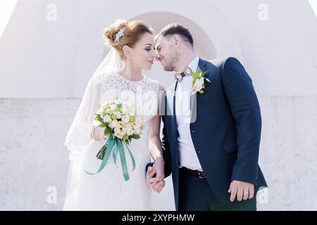 Porträt eines wunderbaren Paares, das an einem Hochzeitstag mit einem Blumenstrauß in der Hand vor dem Hintergrund eines orthodoxen christlichen Denkmals mit Engeln verbrachte. Stockfoto