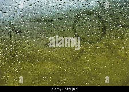 Close-up Sommerregen-Inschrift auf schwitzigem Glas. Sonne- und Sommersymbol auf grünem, verschwommenem Hintergrund Stockfoto