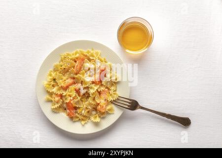 Geräucherter Lachs mit bowtie Pasta. Farfalle mit Lachs und Sahnesoße, Schuß von der Oberseite auf weißem Leinen Tischdecke mit einer Gabel, ein Glas Wein, ein Stockfoto