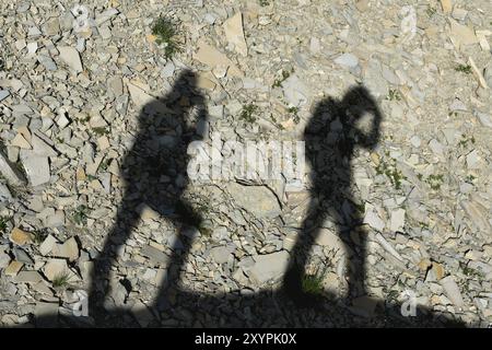 Zwei Schatten von Fotografen auf der Erde, die bergauf gehen. Silhouetten von zwei Personen, die bergauf gehen Stockfoto