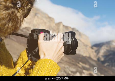 Eine Touristenfotografin mit Pelzmütze und gelbem Pullover in den Bergen macht Fotos mit ihrer Digitalkamera. Der Begriff der Fotografie auf der Reise Stockfoto