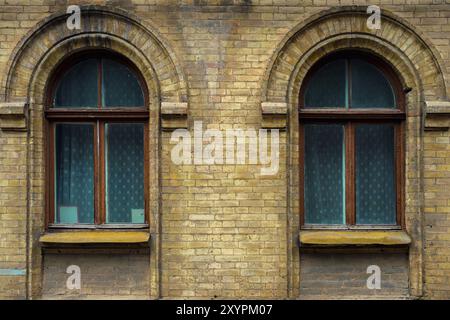 Zwei alte Bogenfenster in einer Wand aus gelben Ziegeln. Grün, die Farben von Meereswellen-Glas in einem braunen dunkelroten Holzrahmen. Das Konzept des antiken V Stockfoto