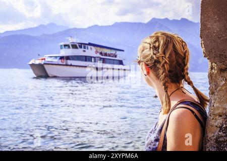 Autofähre am gardasee, Abend. Das junge Mädchen beobachtet die Fähre, das Wasser und die Berge im Hintergrund Stockfoto