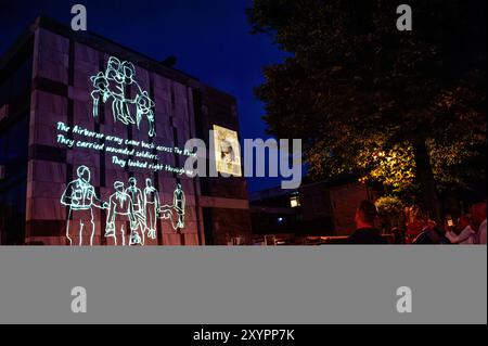 Arnhem, Gelderland, Niederlande. August 2024. Man sieht die Geschichten über den Zweiten Weltkrieg, die an die Wand eines Gebäudes projiziert werden. An die 80. Schlacht von Arnheim erinnert man, in der Abenddämmerung erleuchten spezielle Projektionen Gebäude im Stadtzentrum. Die Schlacht bei Arnheim wurde während der Operation Market Garden ausgetragen. Die Operation Market sollte die deutschen Truppen überraschen und Arnheim und seine wichtigen Brücken über den Rhein erobern, bevor sie von den Verteidigern zerstört werden konnten. Es war der größte Luftangriff in der Geschichte und einer der ehrgeizigsten alliierten Operationen des Zweiten Weltkriegs Stockfoto