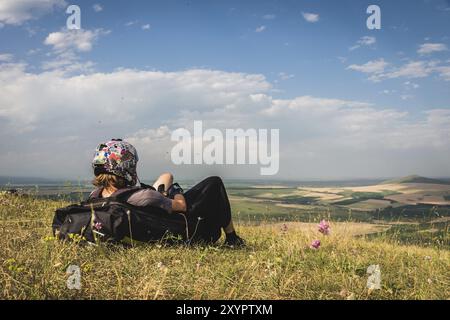 Ein professioneller Gleitschirm in voller Ausrüstung und ein Helm liegt und ruht auf dem Gras hoch in den Bergen und schaut auf die Wolken Stockfoto