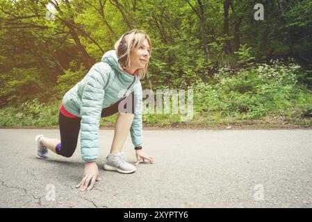 Athletische Frau läuft auf dem Land Straße. Fitness-Lauferin in bereit Startlinie Pose im Sommer Sprint Herausforderung Stockfoto