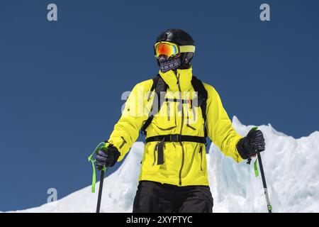 Skifahrer, der auf einer Piste steht. Mann in einem leichten Anzug, Helm und Maske beim Skifahren ist Ski fahren. Im Hintergrund schneebedeckte Berge, Skifahrer, Kaukasus MoU Stockfoto