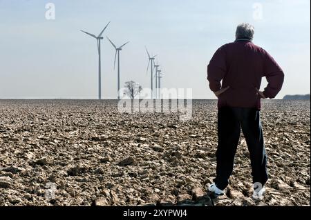 Der Mann steht auf einem Feld und schaut sich Windräder an Stockfoto