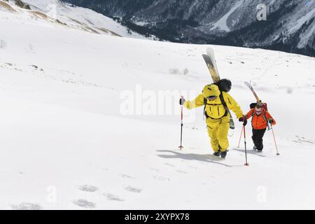 Zwei Ski Freerider klettern die Piste in Tiefschneepulver, wobei die Ausrüstung auf der Rückseite auf dem Rucksack befestigt ist. Das Konzept des Winterextremen Sports Stockfoto