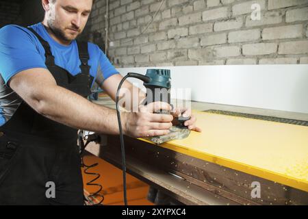 Der professionelle Zimmermann verarbeitet die Kunststoffkanten der Arbeitsplatte mit einem speziellen Elektrowerkzeug Stockfoto