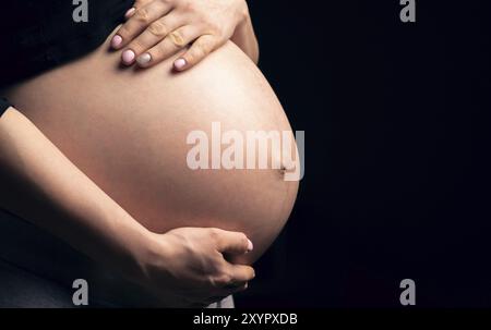 Bauch einer schwangeren Frau von der Seite. Dunkler Hintergrund, Kopierbereich Stockfoto