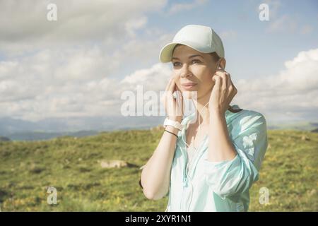 Fitness-Läuferin, die Musik über die Natur hört. Porträt eines schönen Mädchens mit Ohrhörern und Laufkappe. Vor dem Hintergrund von Stockfoto