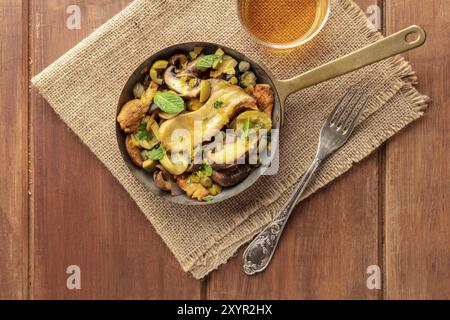 Rustikale Pilze und Oliven saute mit Minze, mit einem Glas Weißwein, Schuß von oben auf einen dunklen rustikalen Hintergrund mit Kopie Raum Stockfoto