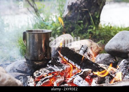 Die kochende Flüssigkeit in einem Edelstahlbecher steht auf Steinen mit Kohlen im Feuer Stockfoto