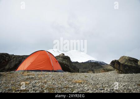 Ein orangenes Hochgebirgszelt befindet sich zwischen Steinen hoch in den Bergen des Kaukasus vor dem Hintergrund des Kaukasus. Glade aus Stein m Stockfoto