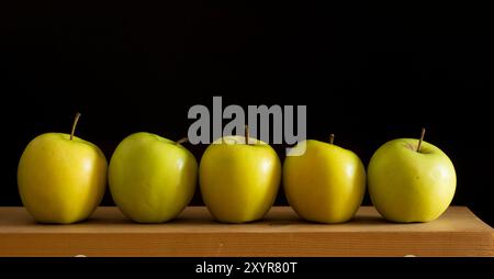 Alle verschieden, alle gleich - fünf Äpfel hintereinander über Holztisch vor schwarzem Hintergrund Stockfoto