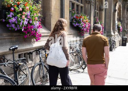 Rückansicht eines Mannes von zwei Personen, der die Straße entlang ging, mit wunderschönen hängenden Körben und Fahrrädern, die an die Gebäudewand im Stadtzentrum von Oxford, Großbritannien, lehnten Stockfoto