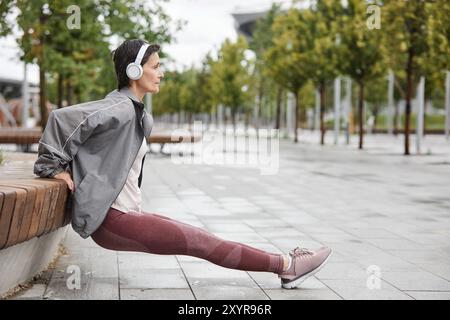 Seitenansicht einer älteren Frau mit Kopfhörern, die regelmäßig im Stadtpark mit Fliesen und Kopierraum trainieren Stockfoto