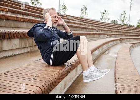 Seitenansicht eines athletischen älteren Mannes in Sportbekleidung, der Crunches auf der Bank macht und die bauchmuskulatur während des täglichen Workouts im Stadtpark stärkt, Kopierraum Stockfoto