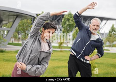 Mittlere Aufnahme einer älteren Frau und eines Mannes, die sich beim gemeinsamen Workout im Morning City Park aufwärmen Stockfoto