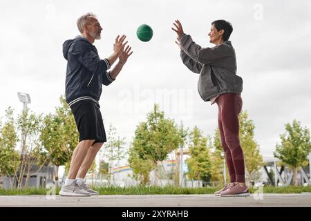 Seitenansicht einer lächelnden Frau und eines Mannes in Sportbekleidung, die Squat-Sprünge am Ball machen Stockfoto