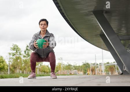 Ein vollständiger Schuss einer Frau, die den Ball in statischer Hockposition hält und im Stadtpark vor grauem Herbsthimmel trainiert, Kopierraum Stockfoto