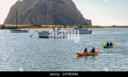 Morro Bay, Kalifornien, USA. Juli 2024. Die Menschen genießen Kajaktouren in ruhigen Gewässern neben verankerten Booten und einer felsigen Küste. Stockfoto