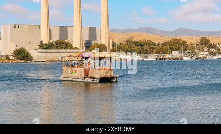 Morro Bay, Kalifornien, USA. Juli 2024. Ein Tiki-Boot bietet Abenteuertouren auf dem Wasser mit einer malerischen Küstenstadt im Hintergrund. Stockfoto