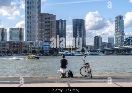 Skyline auf der Nieuwe Maas, Wolkenkratzer, Mann, der eine Pause am Ufer macht, Rotterdam, Niederlande Stockfoto