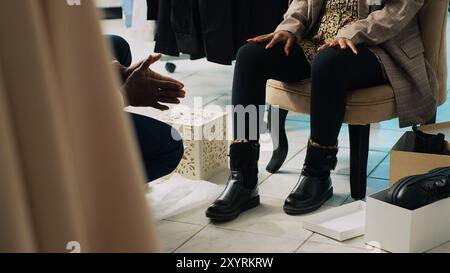 Der Verkäufer empfiehlt ein Paar Stiefel für schwangere Frauen und hilft Ihnen dabei, die perfekte Größe zu finden. afroamerikanischer Kunde probiert Schuhe im Bekleidungsgeschäft an, Konsum. Kamera A.. Stockfoto
