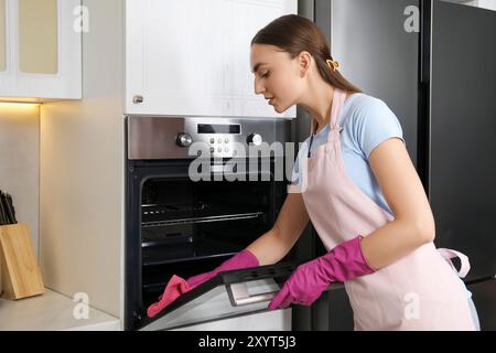 Schöne junge Frau, die den elektrischen Ofen mit Lappen in der Küche abwischt Stockfoto