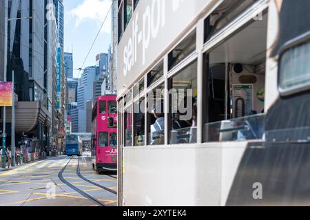 Hongkong, China - 03. Juli 2024 : Eine Hongkonger Straßenbahn, von innen gesehen, mit Passagieren aus dem Fenster. Eine zweite Straßenbahn, rosa und schwarz, Dose Stockfoto