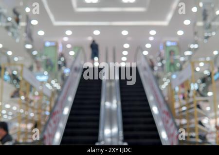 Ein verschwommenes Bild von einem Einkaufszentrum mit Rolltreppen und Leuten, die herumlaufen. Die Szene ist voll und geschäftig, und die Leute gehen ihrem Tag nach. Stockfoto